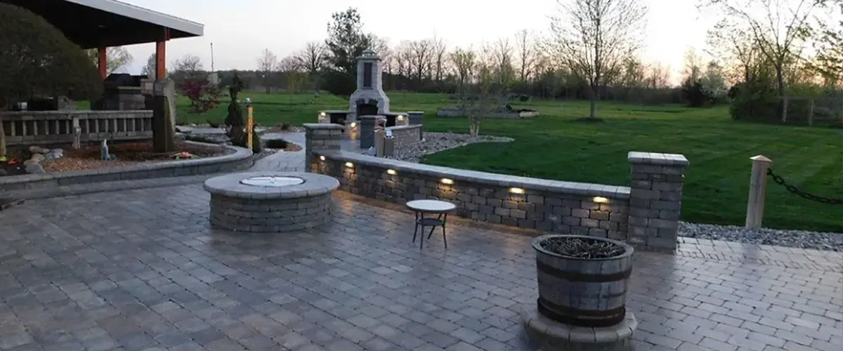 Outdoor living space with pavers floor, fire features, exterior lighting, and fresh, green lawn.