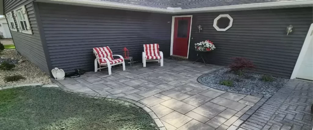 An outdoor living space patio with two red and white striped chairs. A gray home with a red door is in the background.