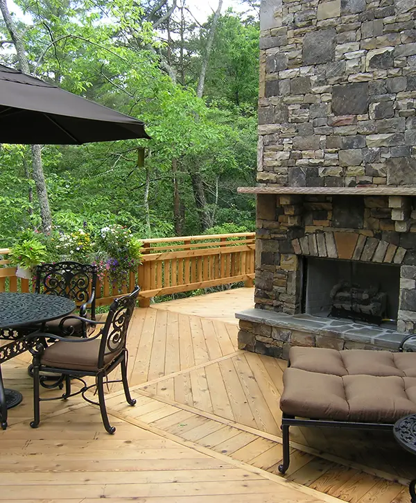 A stone veneer fireplace on a wood deck with outdoor furniture