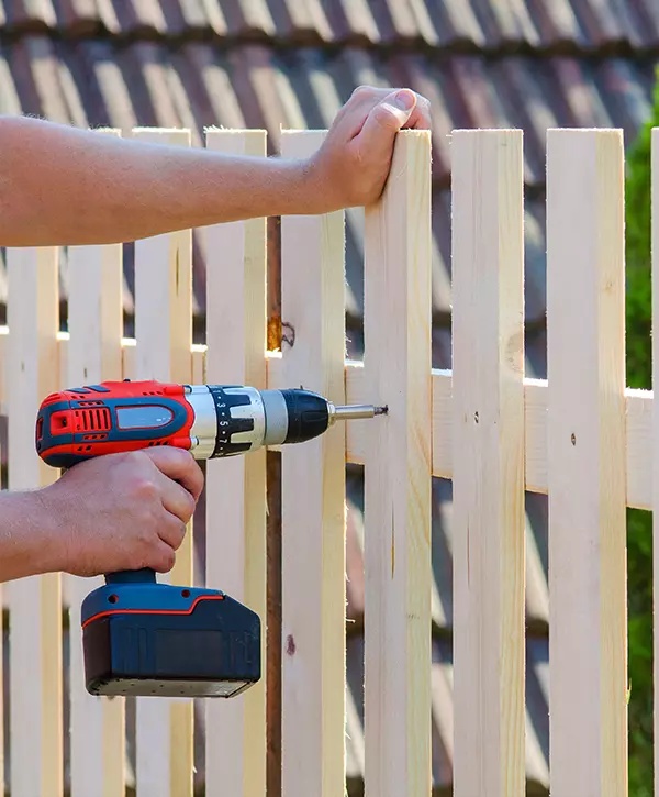 Man hands building wooden fence with a drill and screw