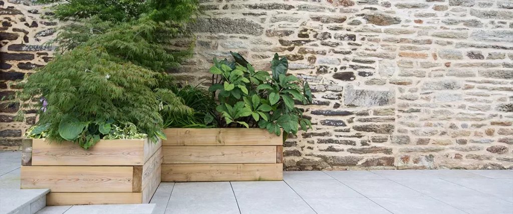 Modern garden design and terrace construction Hillside plot paved with natural sidewalk flagstones in contrast to raised beds planted with green plants in wooden pots in front of an old stone