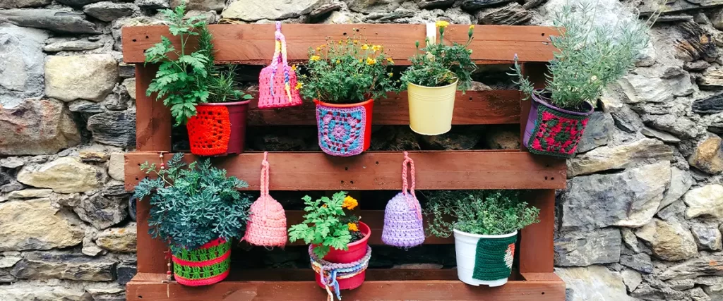 Pots of different bright colors with flowers hanging on a stone wall to decorate the house. Vertical garden. Urban orchard.