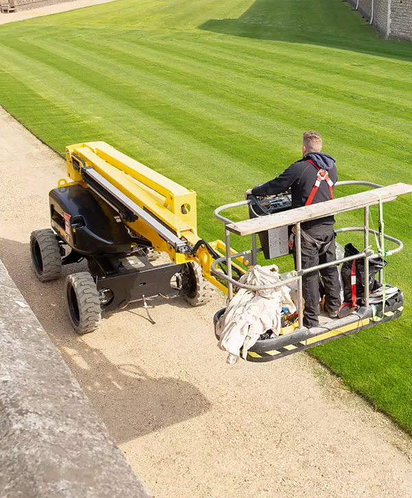 Unidentified gardener cutting the grass of a garden standing on a lawn mower