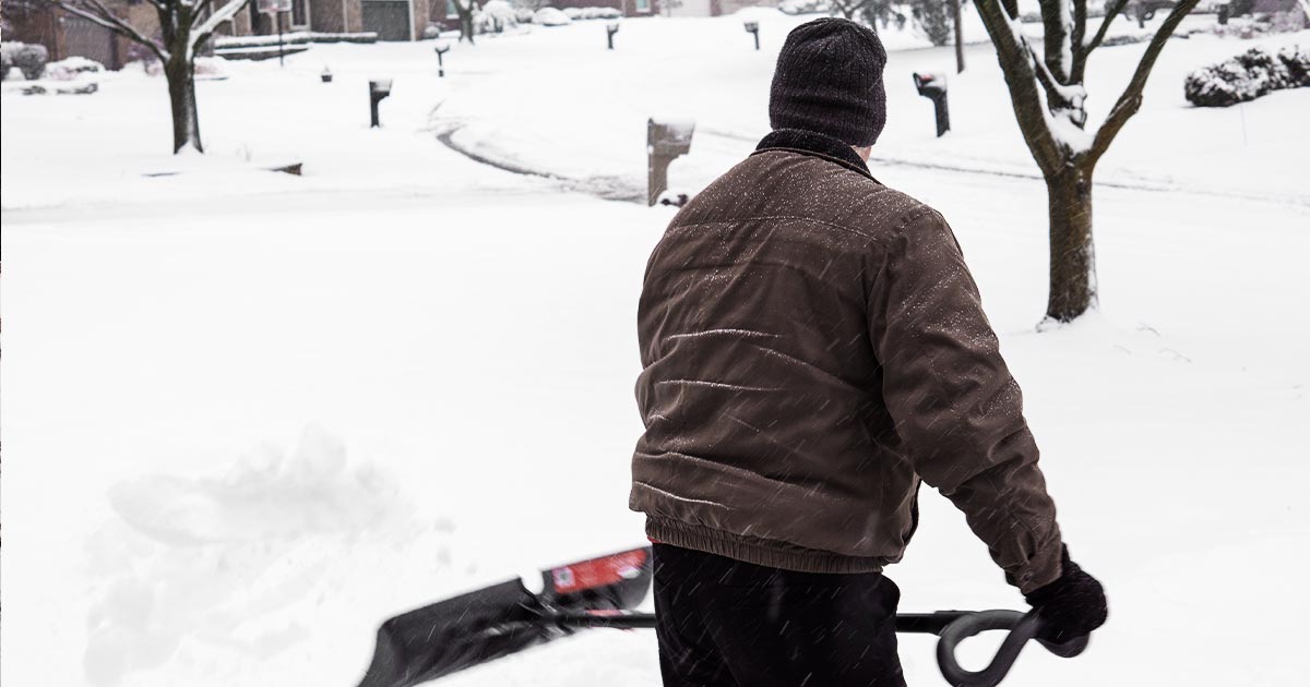 Old man shovels snow from driveway with back turned