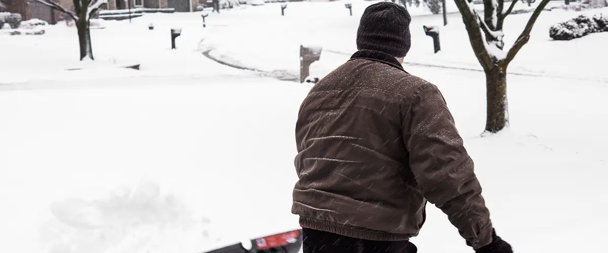 Old man shovels snow from driveway with back turned