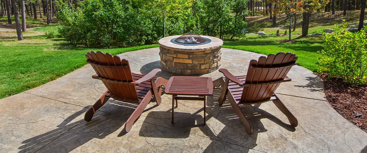 Tranquil outdoor seating area with flagstone patio installation in Bryan, stone fire pit, Adirondack chairs, and lush forest backdrop, perfect for nature relaxation.