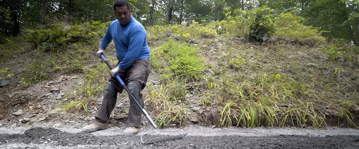 Worker hardscaping in toledo, grading rocky ground for landscaping project.