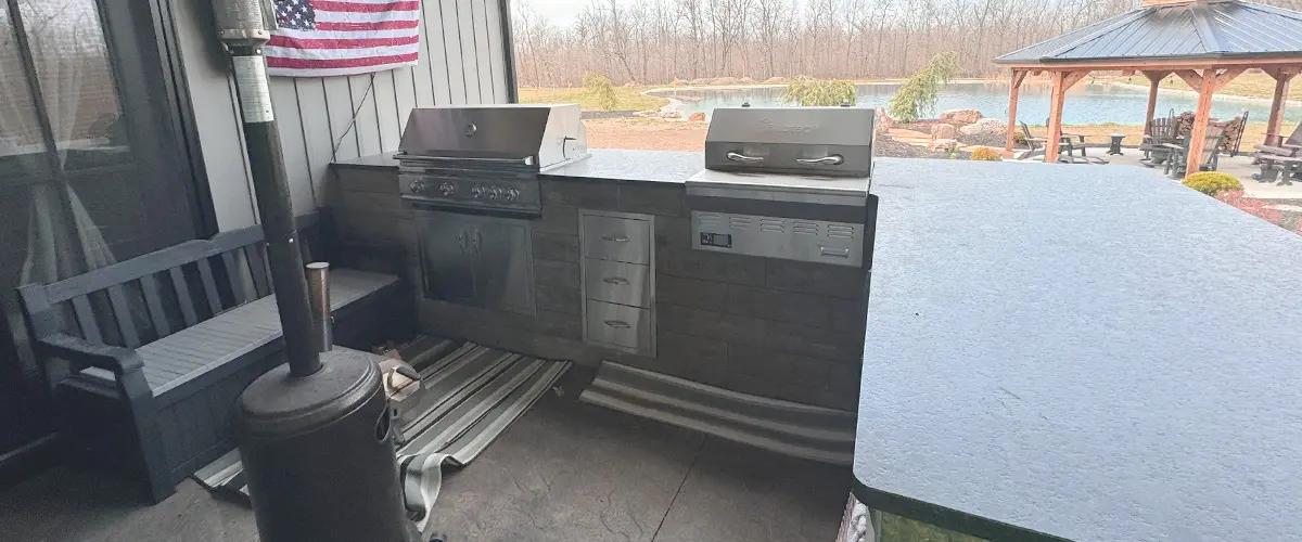 Covered outdoor kitchen with a grill, countertop, and heater, overlooking a scenic pond