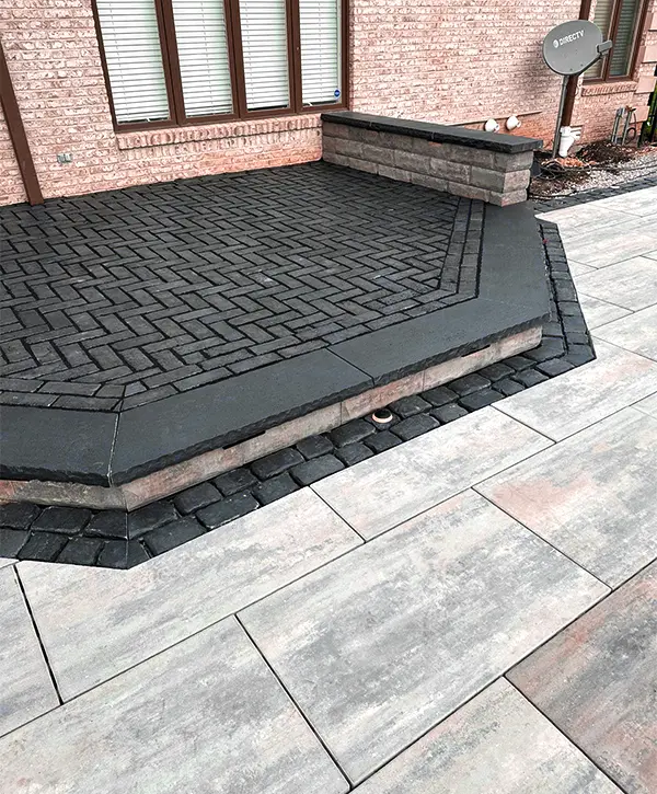 Contemporary outdoor patio featuring a raised brick platform with dark pavers, stone edging, and a stone-tiled floor