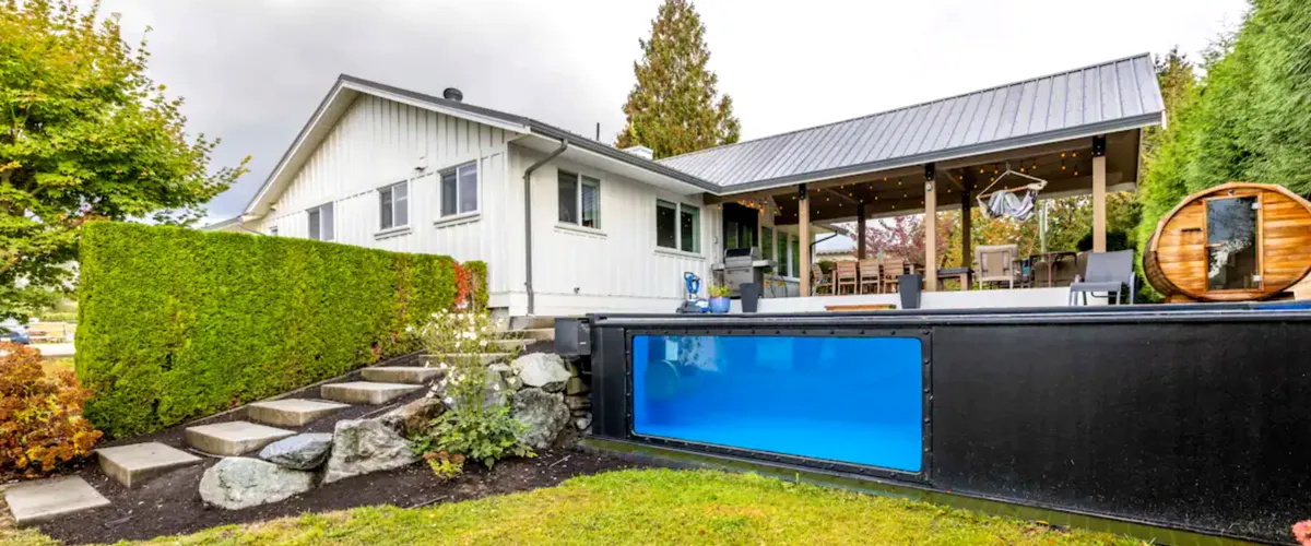 Modern poolside patio with glass fencing and outdoor seating, offering a serene countryside view