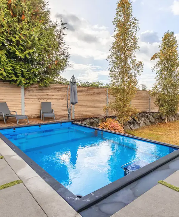 Private backyard with a modern pool, lounge chairs, and lush greenery