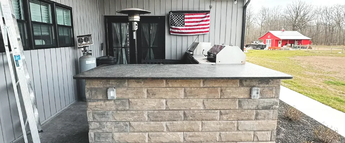 Backyard kitchen with stone bar area and grill under a covered patio